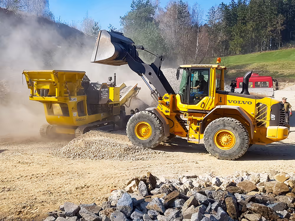 Ein Bagger kippt Steine in die mobile Brechanlage der Firma Brand aus Triftern.
